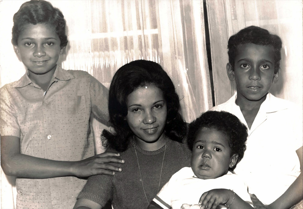Nessa foto em preto e branco, Glaucia olha para a câmera rodeada por três crianças de diferentes idades. O mais velho, à sua direita, está em pé; à sua esquerda, um menino um pouco mais novo, e no seu colo, um bebê.
